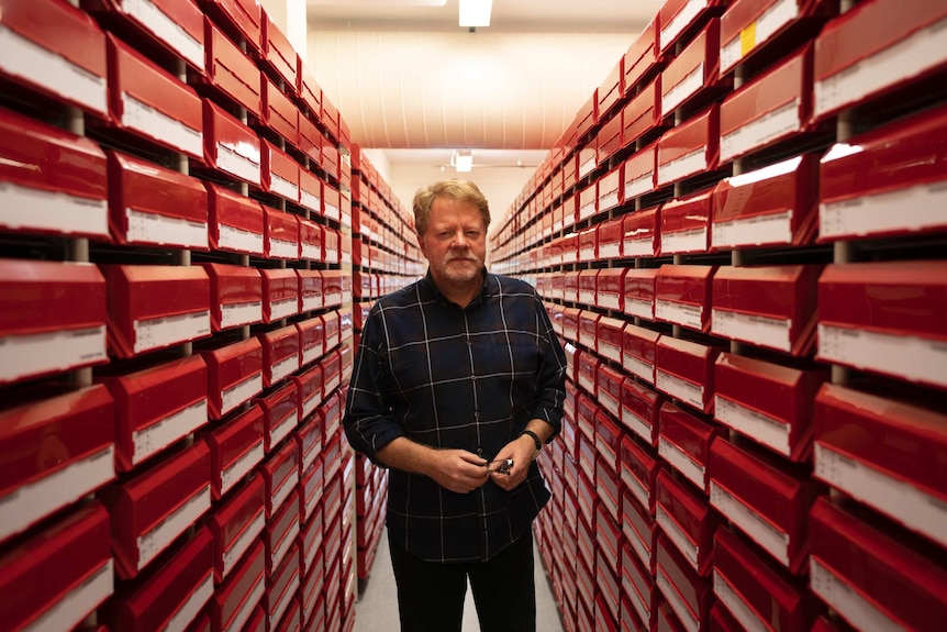 John Huisman stands in an aisle of red shelves.