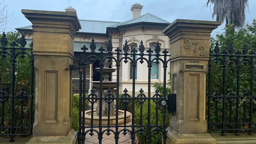 photo of old house from outside front gate with large cement fence posts and white house with arched windows and chimney