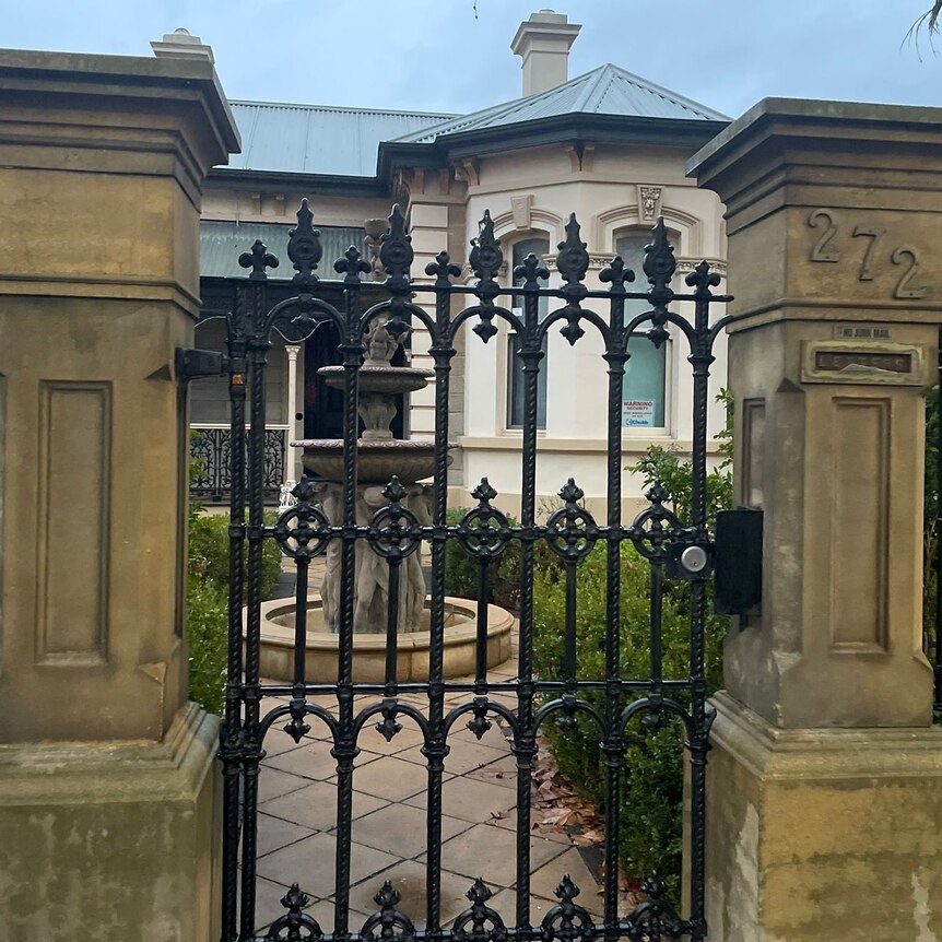 photo of old house from outside front gate with large cement fence posts and white house with arched windows and chimney