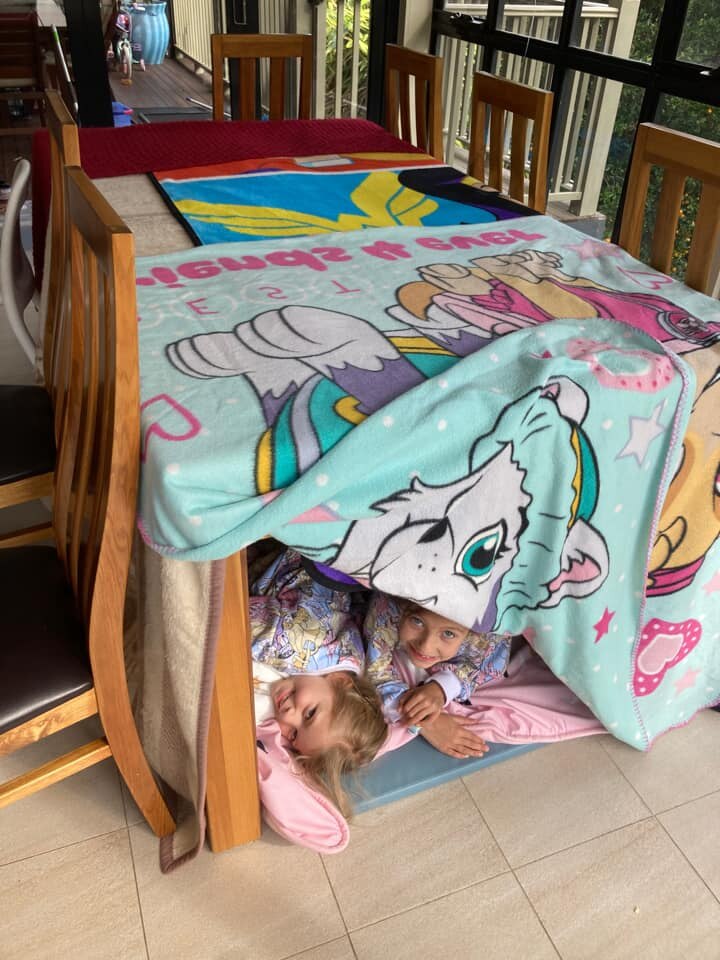 Kids underneath a dining table covered in towels