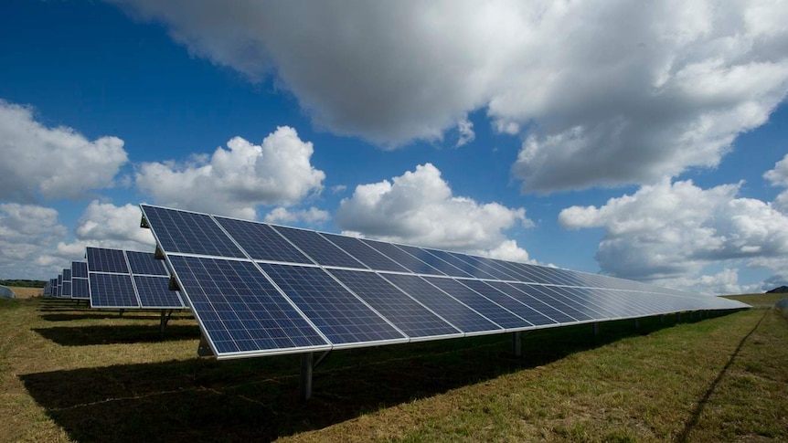 A row of solar panels in a field against a blue cloudy sky.