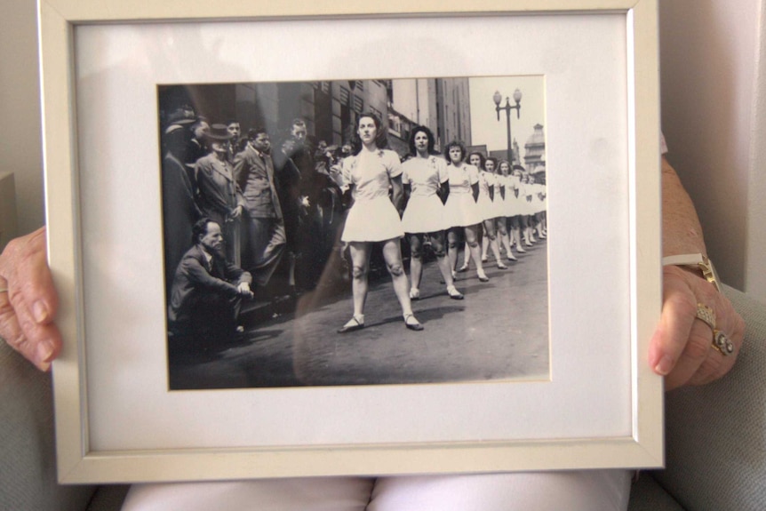 A woman holds a black and white photo in a frame of women in a physical culture competition.
