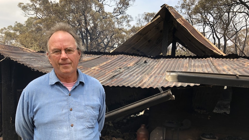 A man standing in front of a burnt-out shed.