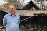 A man standing in front of a burnt-out shed.