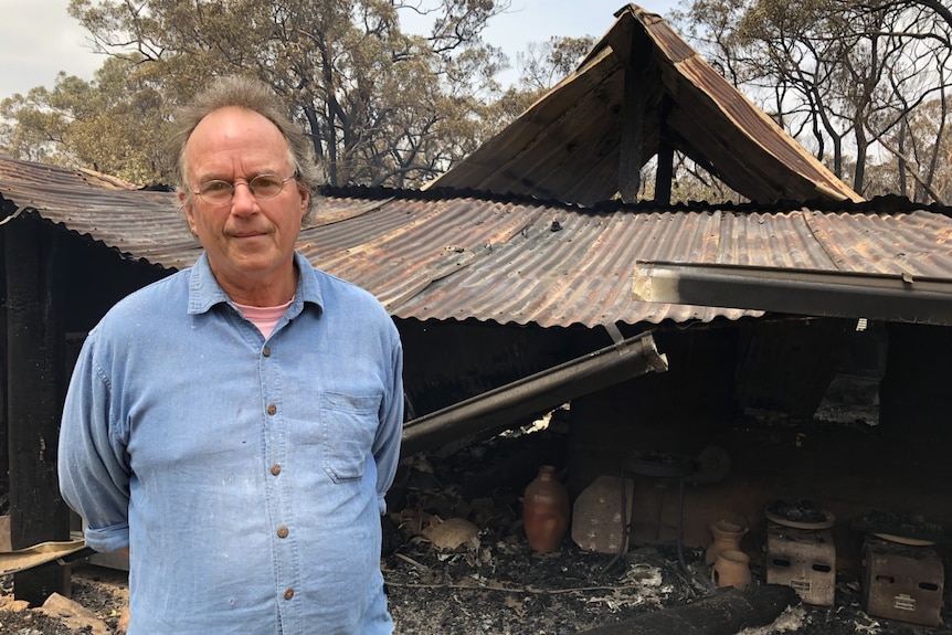 A man standing in front of a burnt-out shed.