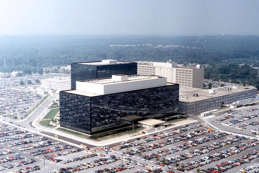 You view a shimmering black rectangular modernist office building ringed by a large concrete carpark.