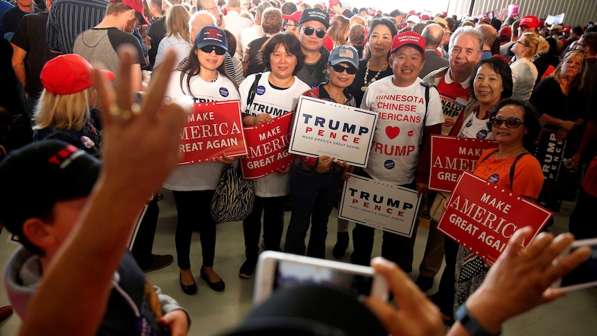 Trump supporters hold signs reading "make america great again" and wear shirts reading "minessata chinese americans heart trump"