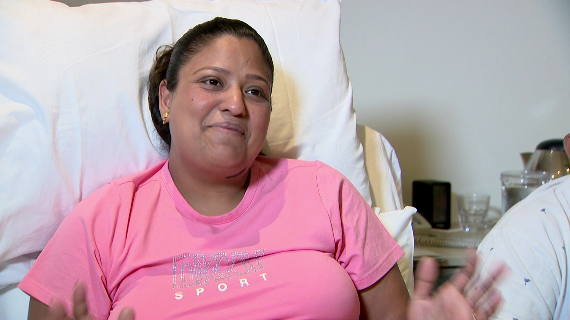 Roshni wearing a pink shirt laying in a hospital bed smiling.