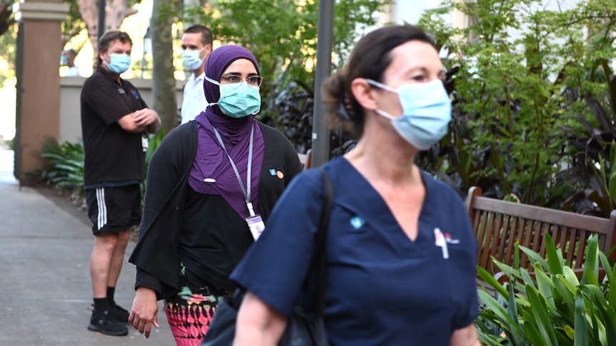 Two women wearing masks walk past two men wearing masks.