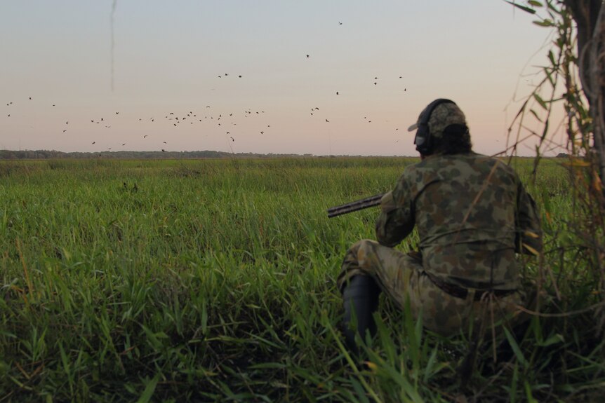 a man in camouflage looking over wetlands.