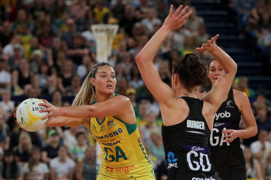 A netballer holds the ball out away from defenders while eyeing off a pass in an international.