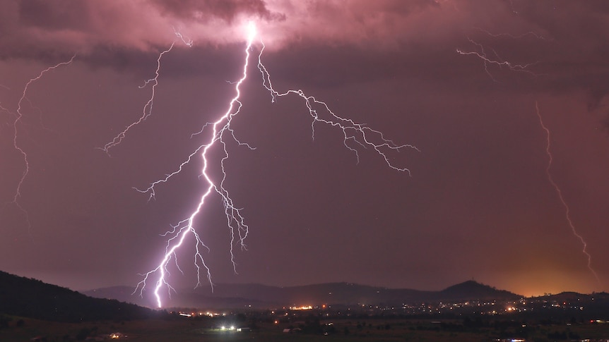 Forked kightning erupts over a darkened valley, reaching from the clouds to the ground   