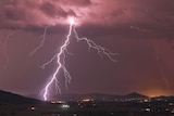 Forked kightning erupts over a darkened valley, reaching from the clouds to the ground   