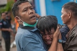 A visibly distraught man is comforted by another man after after identifying his relative among the bodies of tsunami victims.