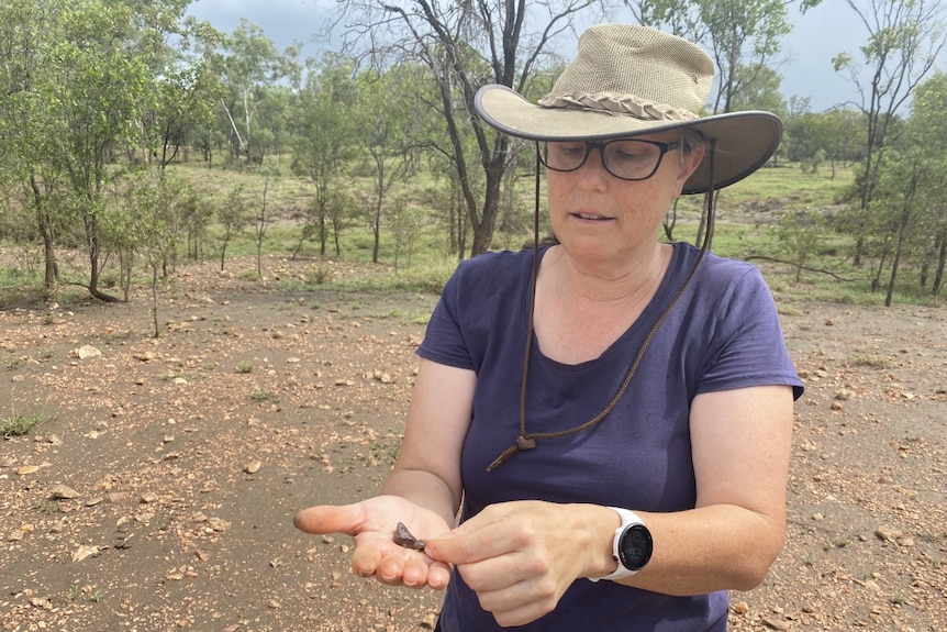 A woman in a hat with a navy shirt is holding rocks in her hands. 