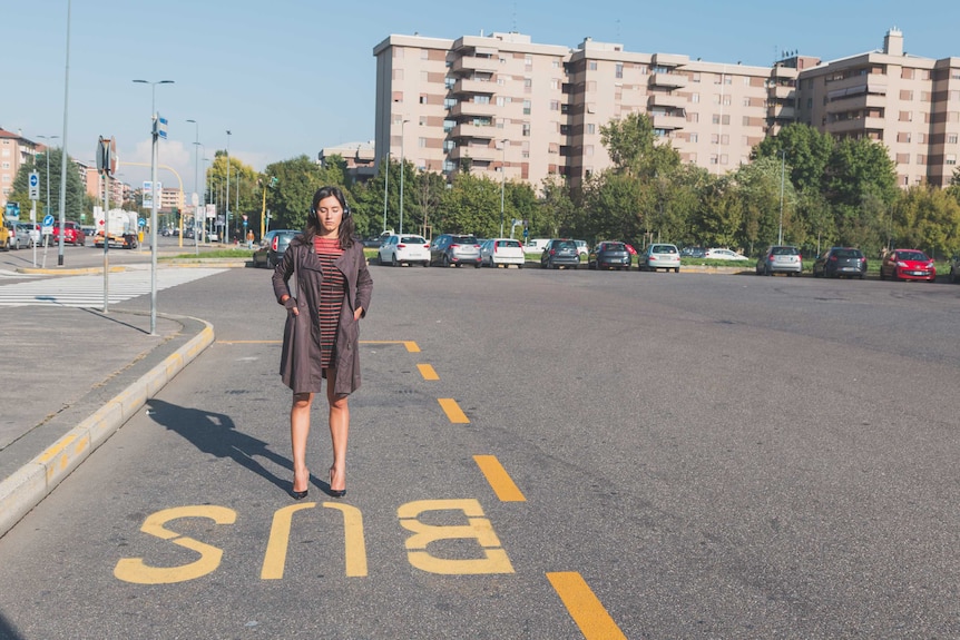 A woman stands at a bus stop.