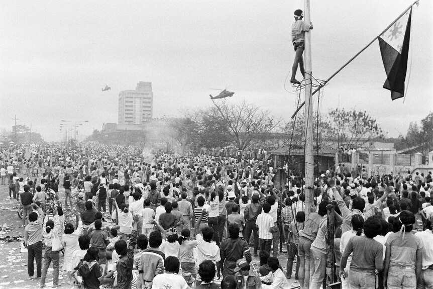 A black and white photo of thousands of people in a street, as helicopters fly past.