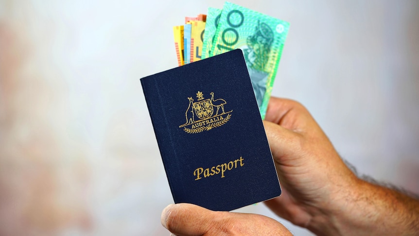 A man holding an Australian passport with 100 and 50 dollar notes Australian money poking out of the passport