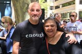 A woman with sunglasses on her head hugging a man with a shirt that reads 'enough'