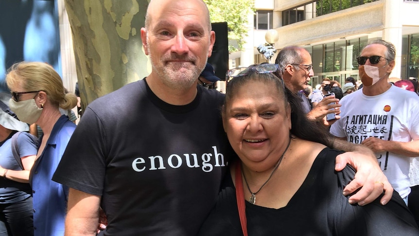 A woman with sunglasses on her head hugging a man with a shirt that reads 'enough'