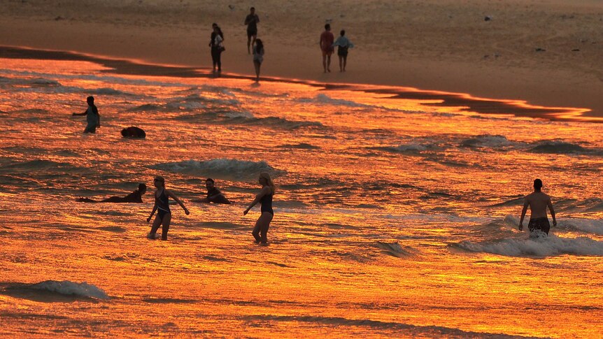 The ocean at Bondi Beach turns red at sunset, while surfers and swimmers enjoy the waves