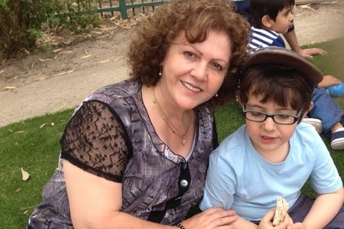 Sonia Sofianopoulos smiling while sitting on grass with her grandson Adam who is eating a sandwich