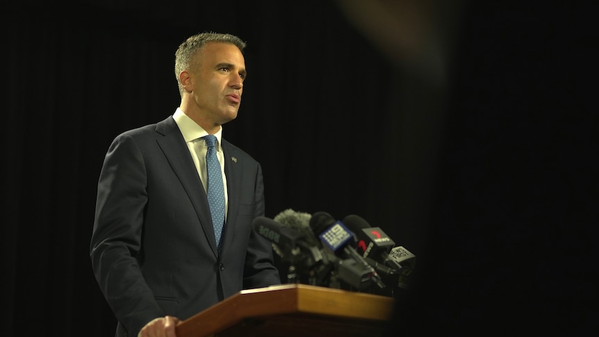 A man wearing a suit and tie at a dais with microphones attached to it