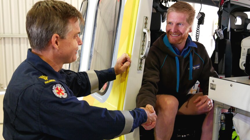 A man sitting inside a helicopter shaking the hand of a paramedic in uniform
