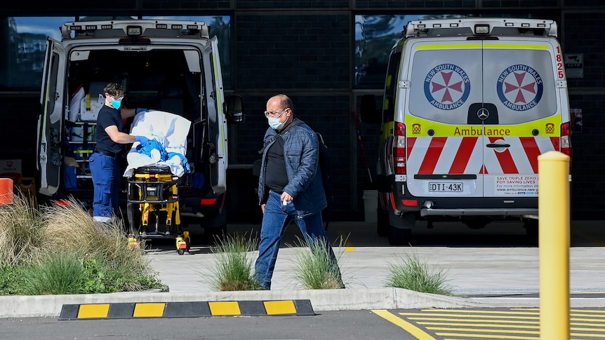 a man wearing a mask walking in front of an ambulance