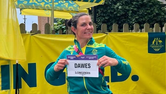 Para-athlete Christie Dawes, smiling in her Australian uniform and holding her Birmingham Commonwealth Games name tag.