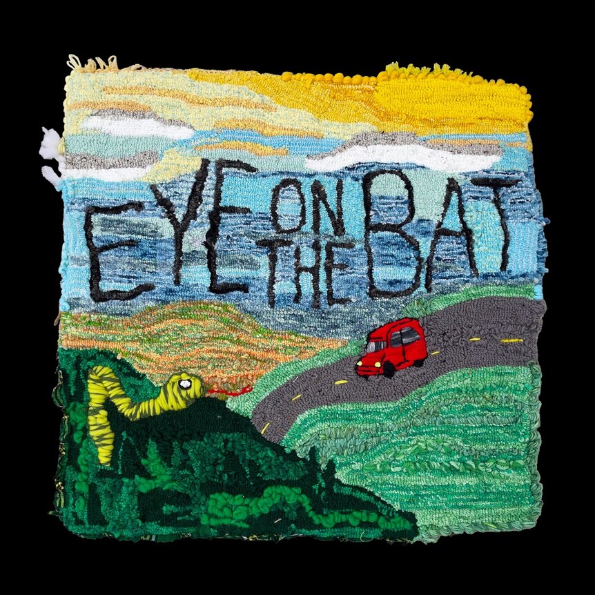 a knitted picture showing a car driving on a country road and a caterpillar 