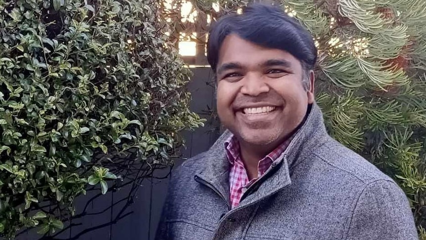 Pradeep Sornaraj in a grey jacket and red checked shirt smiling at camera
