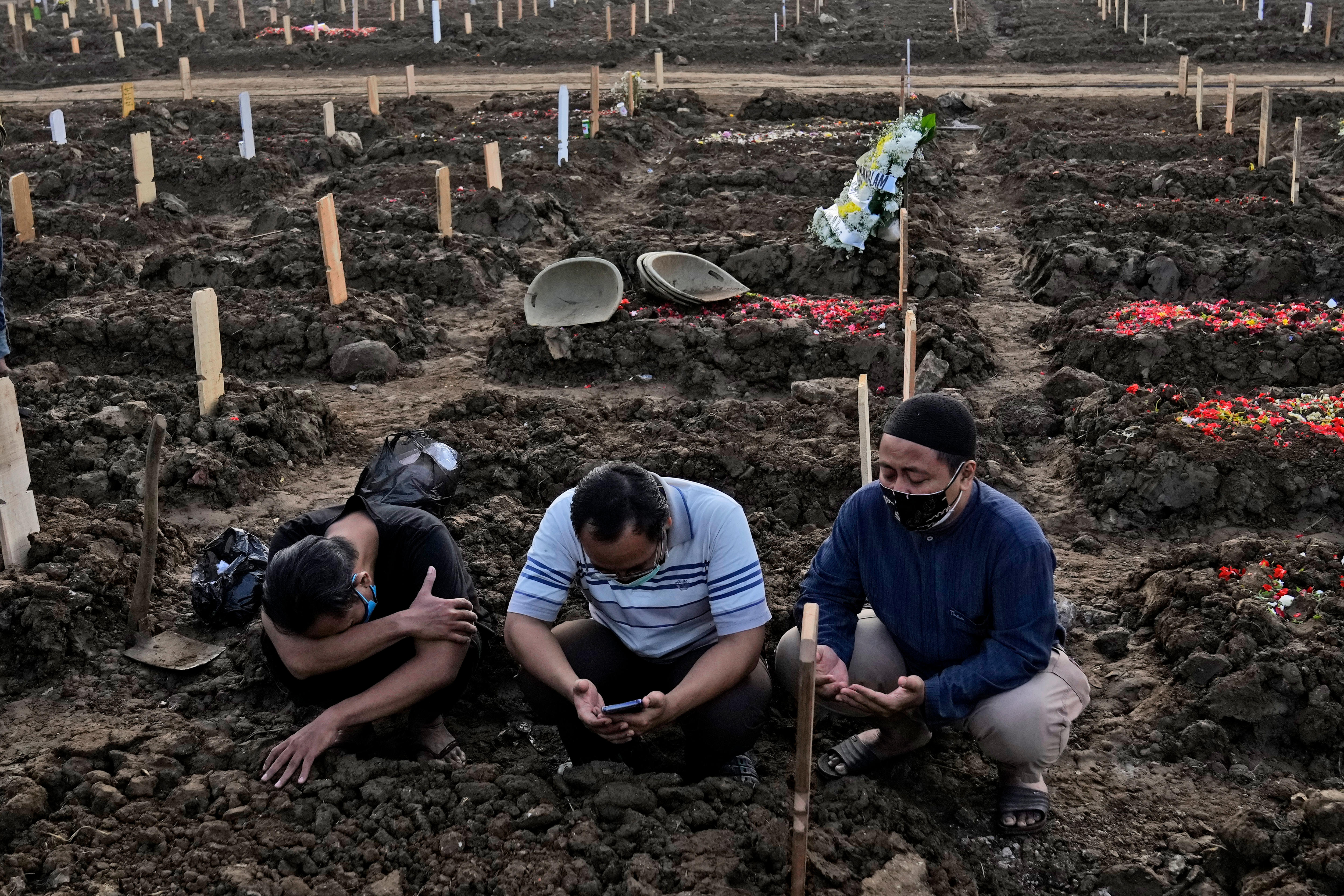 Men pray during the burial of a relative at a cemetery