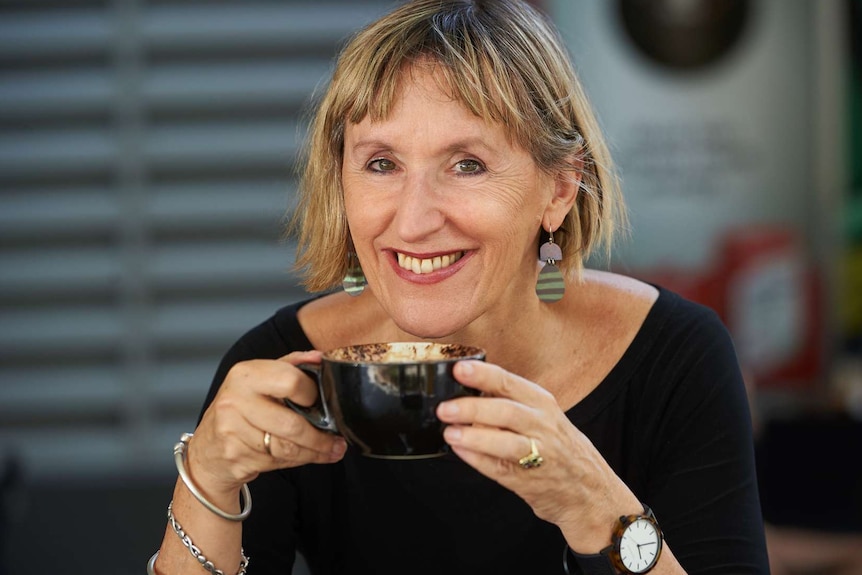 Lady drinking coffee with bright earrings on.