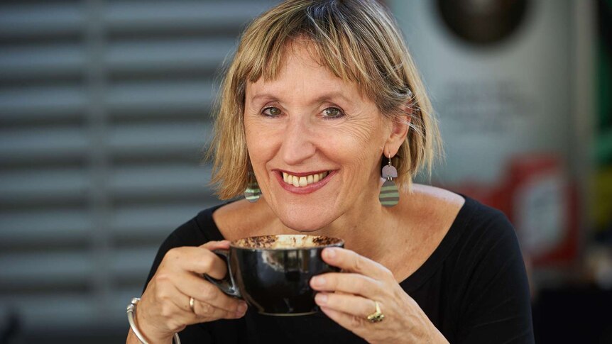 Lady drinking coffee with bright earrings on.