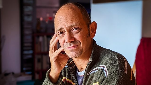 Interior shot of 57-year-old balding man resting his hand against his cheek, looking at camera.