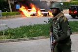A Kenyan soldier holding a gun, while cars behind him burn