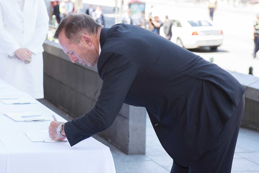Former prime minister Tony Abbott signs the condolence book on arrival for the state funeral service for Ron Walker.