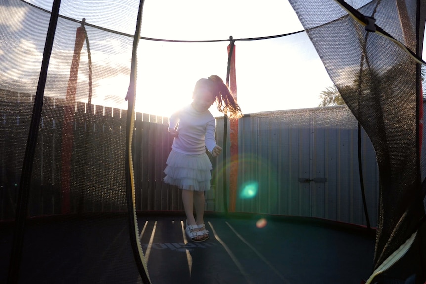Arlo, a silhouette, jumping on a trampoline, sun shining behind her.