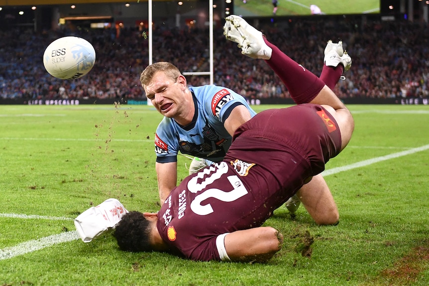 NSW Blues player Tom Trbojevic pushes Queensland Maroons player Xavier Coates over the sideline. Coates head is on the ground.