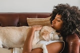 Woman lays on couch hugging her dog