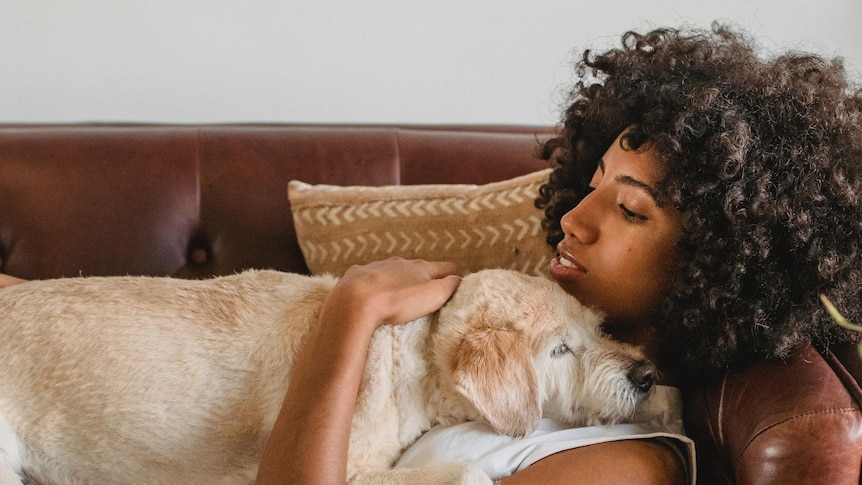 Woman lays on couch hugging her dog