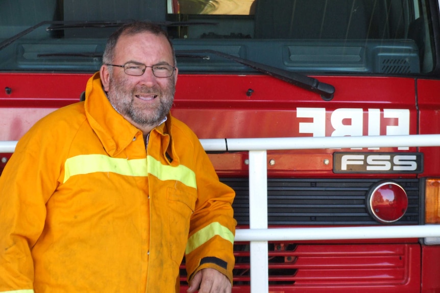 A Country Fire Authority Volunteer stands leaning against a fire truck in his fire gear