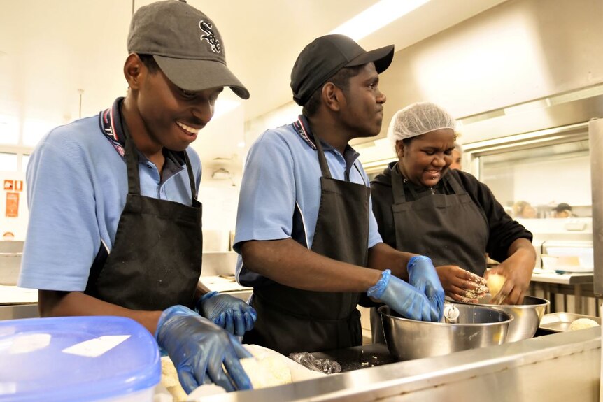 Three Indigenous students smile as they work in the kitchen.