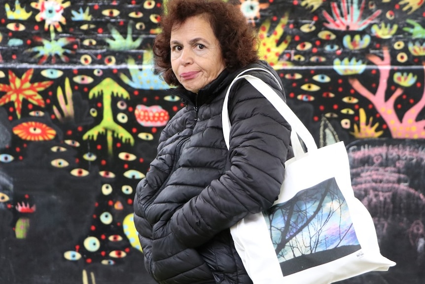 A woman with curly hair carries a tote bag with a photo of trees printed on the front