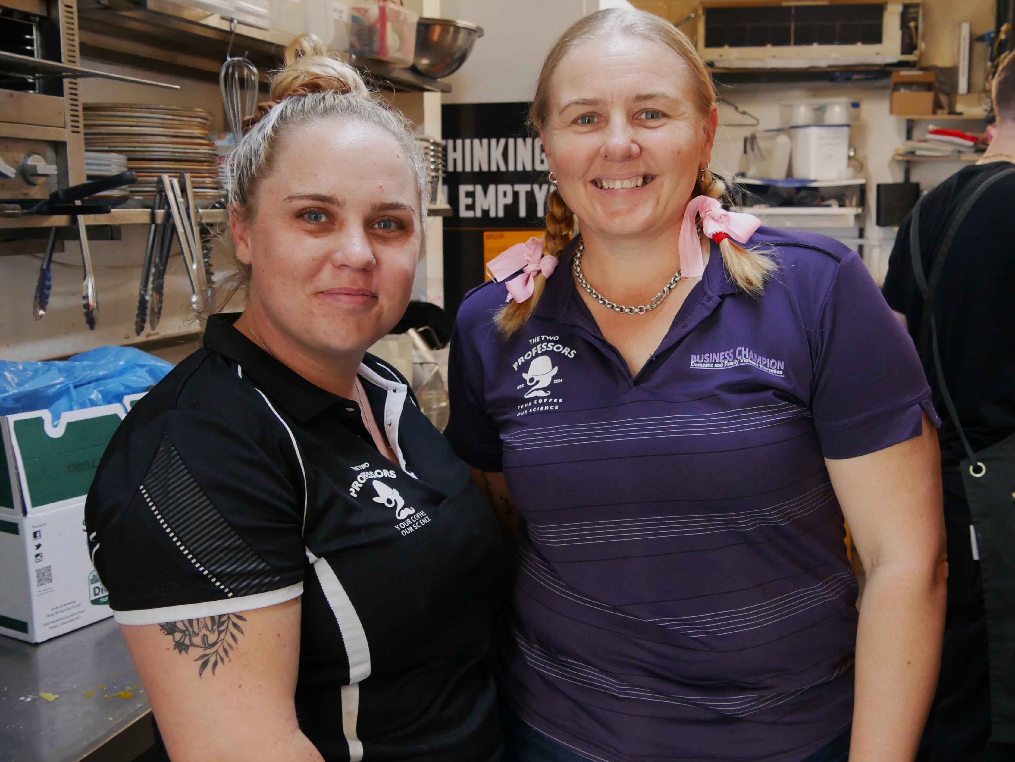 Two young women stand side by side smiling amongst a busy commercial kitchen