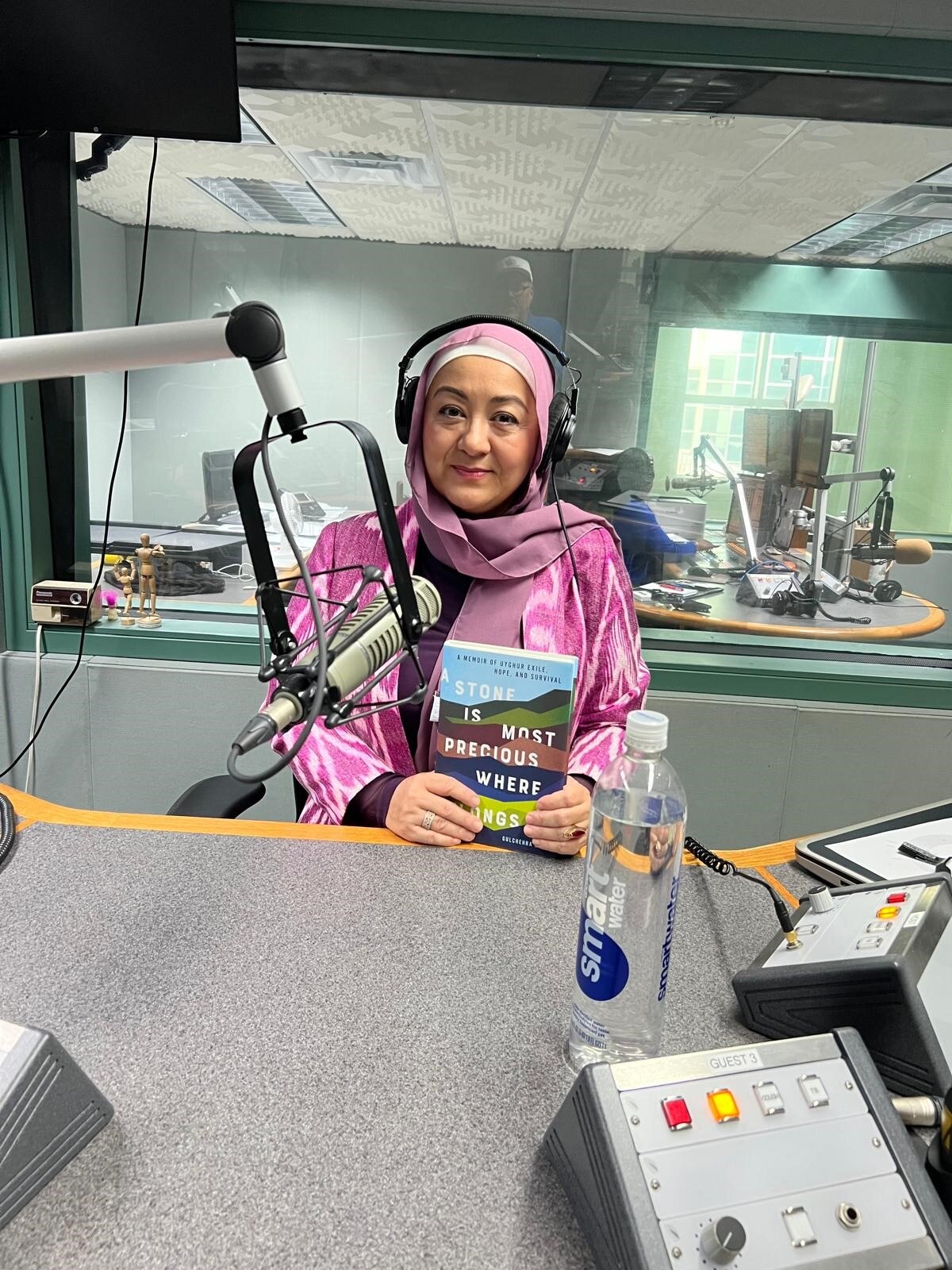 A woman sits in a radio studio holding a book.