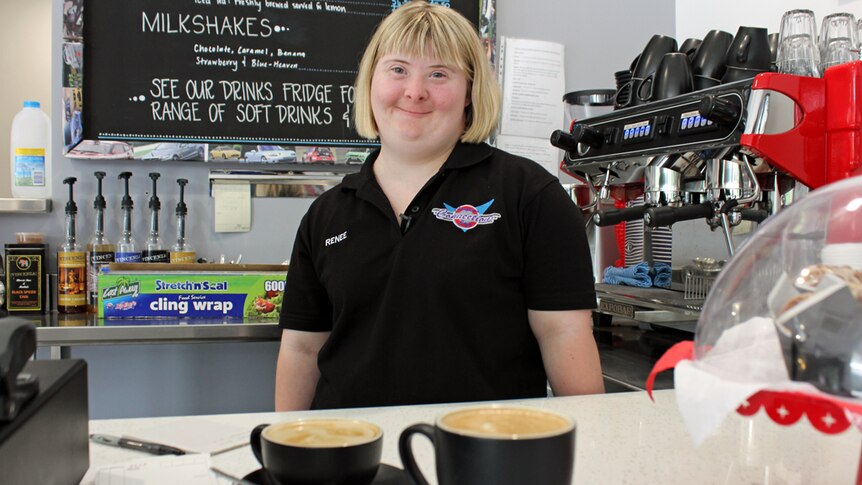 Female trainee stands proudly in front of two cups of coffee.