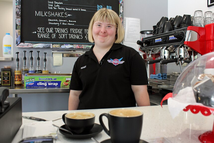 Female trainee stands proudly in front of two cups of coffee.