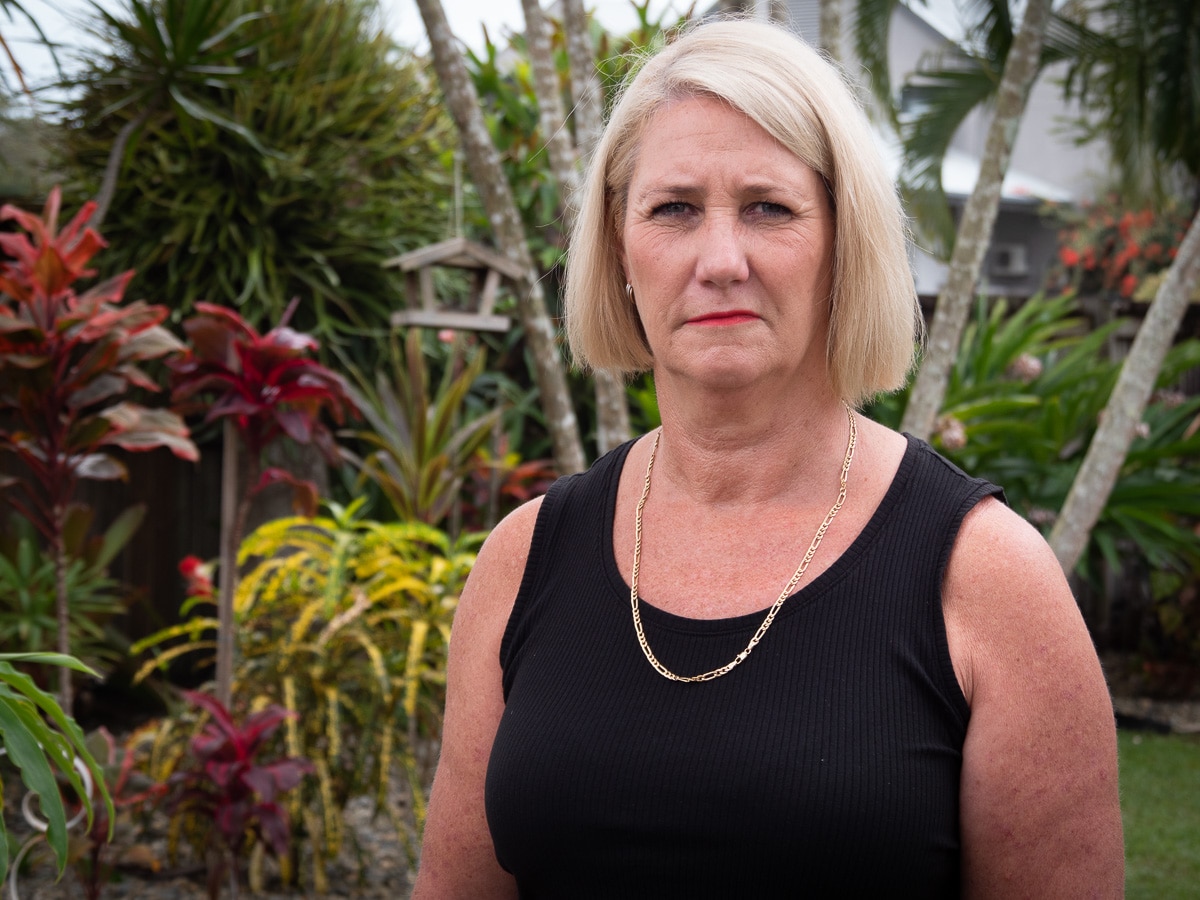 A woman stands on a palm tree beach and looks directly at the camera
